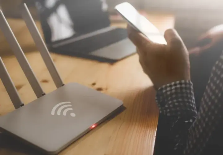 Router i osoba trzymająca telefon, zastanawiająca się, dlaczego wifi samo się wyłącza w telefonie.