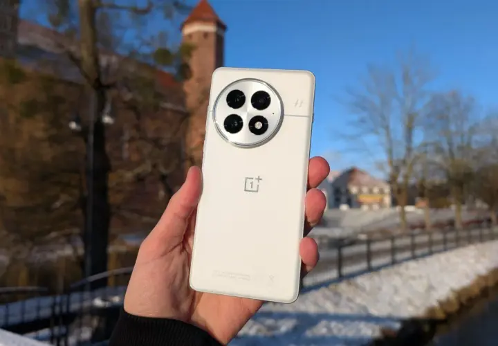Biały smartfon z charakterystycznym modułem aparatów, trzymany na tle zimowego krajobrazu z zamkiem. System Oxygen OS działa płynnie.