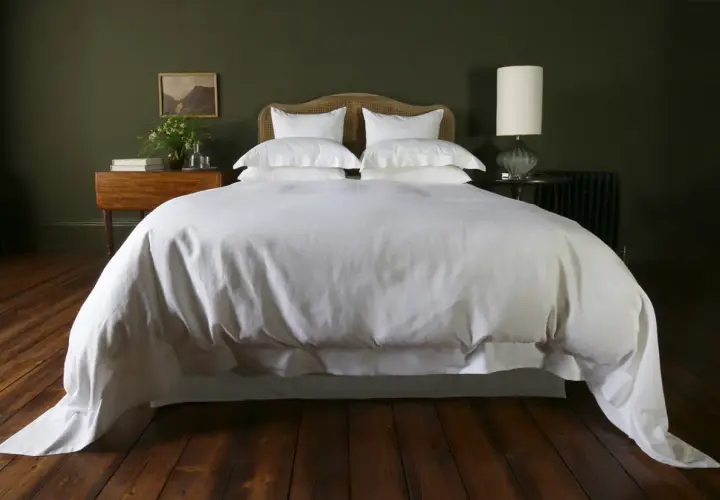 A white duvet cover, resembling a plush bedspread, drapes over a neatly made bed, contrasting with the crisp bed sheet visible beneath.