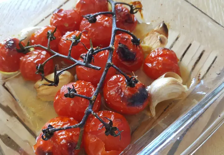 Tomates cerises au four, caramélisées et parfumées à l'ail, dans un plat en verre.