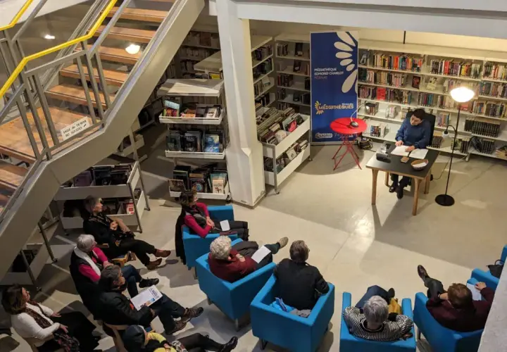 Une bibliothécaire présente un livre à un public assis. Une gestion des actifs numériques efficace permet de retrouver facilement ce type de contenu.