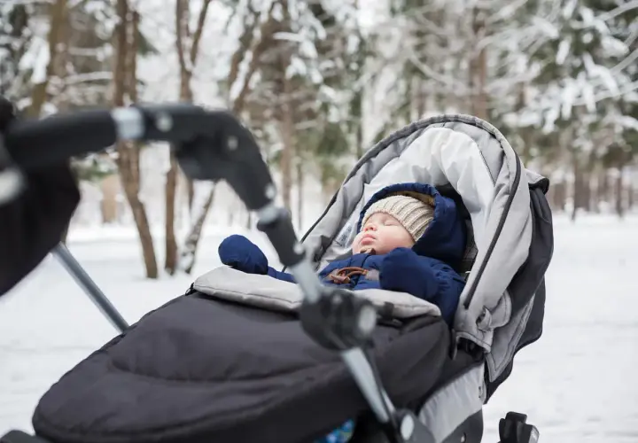 Słodki niemowlak śpi w wózku podczas zimowego spaceru. Otulony ciepłym kombinezonem i czapką, odpoczywa wśród zaśnieżonych drzew.