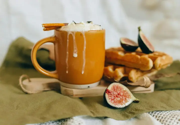 En varm kopp chai latte med vispad grädde och kanelstång, bredvid nybakade våfflor och färska fikon. Perfekt för ett mysigt chai latte recept.
