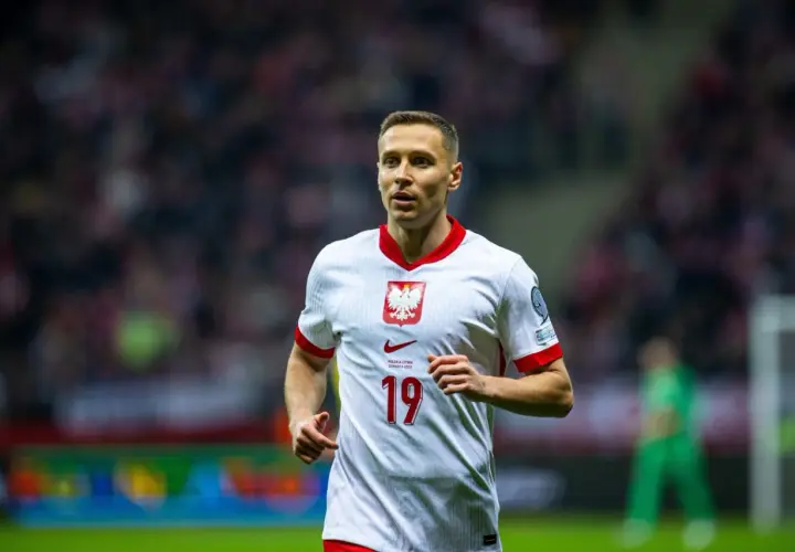 Frankowski piłkarz w białej koszulce z orłem na piersi, numer 19. Biegnie po boisku, skupiony na grze.
