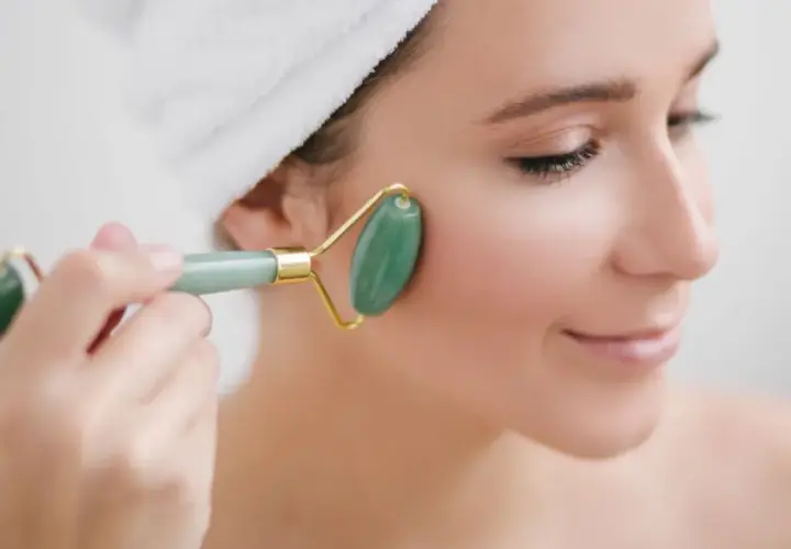 En kvinna med handduk i håret använder en grön jade roller för ansiktet.