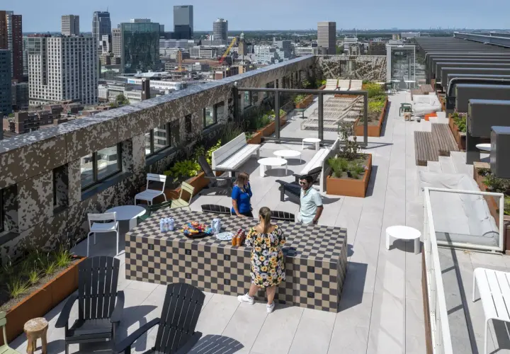 Ein begehbarer Flachdachgarten mit Stadtblick. Menschen entspannen sich auf der Dachterrasse, die mit Sitzgelegenheiten, Pflanzen und einem Schachbrett-Tisch ausgestattet ist.