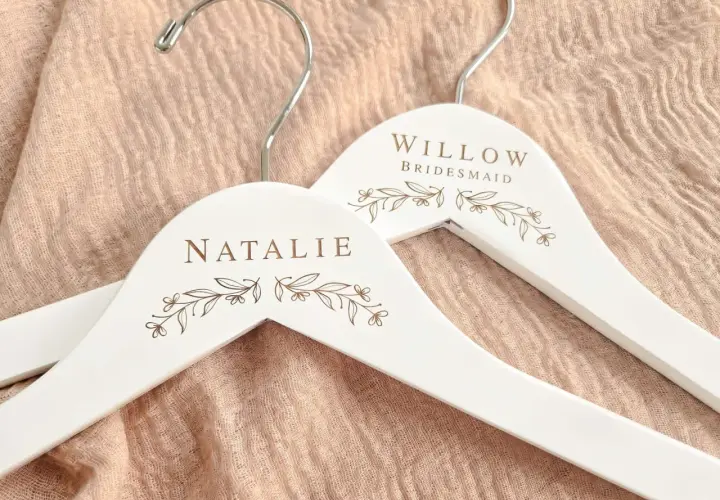 Perchas blancas personalizadas con nombres "Natalie" y "Willow Bridesmaid", adornadas con delicados motivos florales.