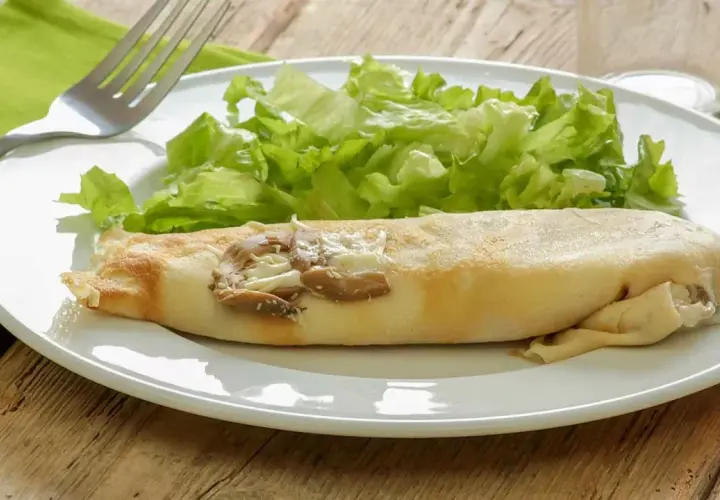 Une ficelle picarde garnie de champignons et de fromage, accompagnée d'une salade verte croquante sur une assiette blanche.