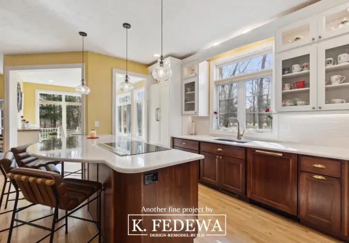A bright, airy kitchen with natural wood cabinets and a large island. Sunlight streams through large windows, illuminating the warm tones of the wood.