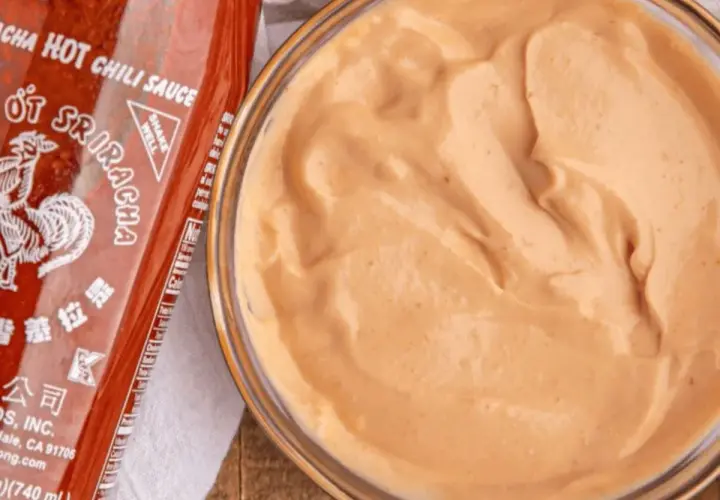 A bowl of creamy, orange spicy mayo recipe sits next to a bottle of Sriracha hot chili sauce.