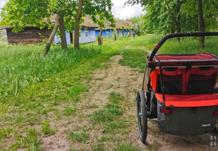 Wózek dziecięcy na tle tradycyjnych, niebieskich chat z krytymi strzechą dachami. Idealne miejsce na wycieczkę, odkrywanie ciekawych miejsc 200 km od Łodzi.