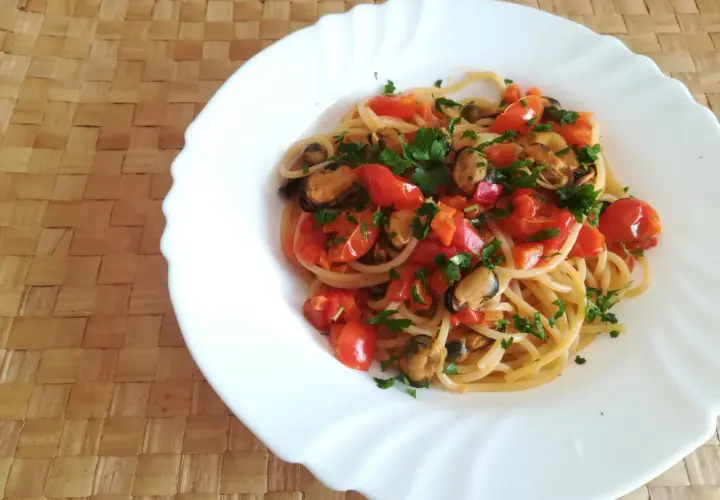 Un piatto di spaghetti con le cozze e pomodorini freschi, guarnito con prezzemolo tritato, pronto per essere gustato.