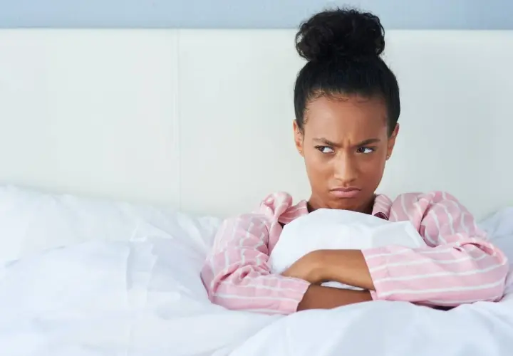 Chica enfadada en la cama, pensando en excusas para no quedar.