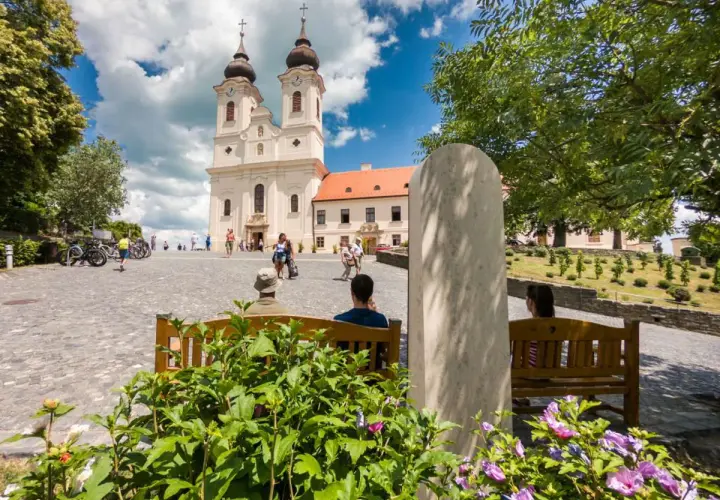 Tihany Balaton: malowniczy plac przed opactwem benedyktynów, z turystami odpoczywającymi na ławkach i podziwiającymi architekturę.