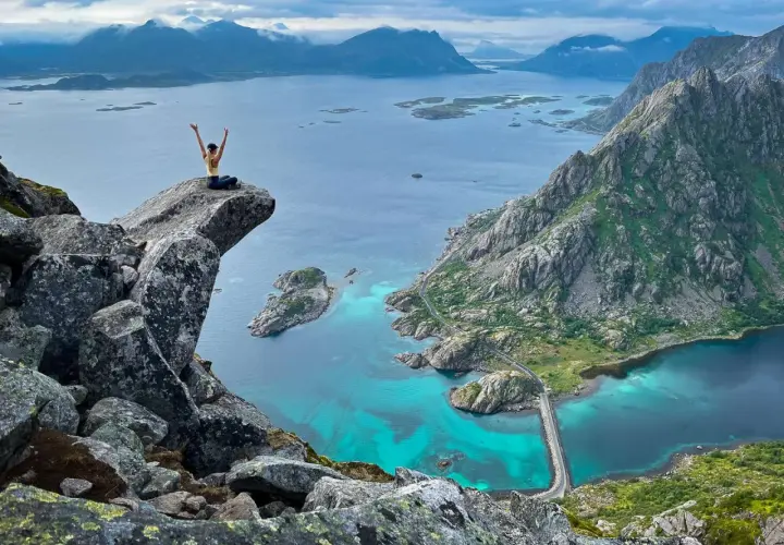 A hiker celebrates on a cliff overlooking turquoise waters and rugged mountains, showcasing some of the best islands for hiking.
