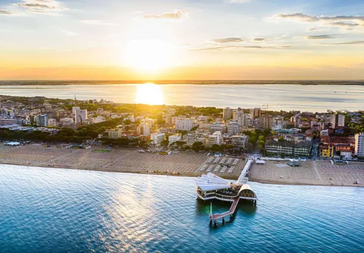 Coucher de soleil sur Lignano, Italie. La plage et la mer s'étendent à perte de vue, avec un pont moderne se jetant dans l'eau.