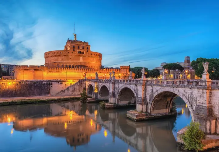 Le Castel Sant'Angelo à Rome, illuminé au crépuscule, se reflète dans le Tibre. Le pont Saint-Ange, orné de statues, mène à cette ancienne forteresse.