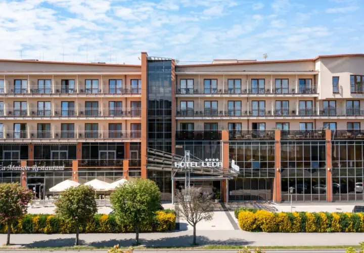 Elegancki hotel Leda Spa z restauracją La Maison, z licznymi balkonami i przeszklonym wejściem, otoczony zielenią.
