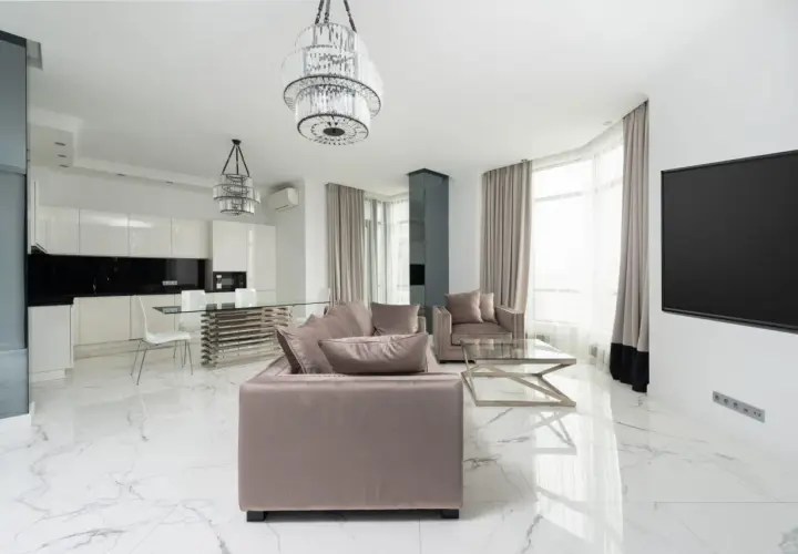 Soggiorno moderno con divani beige, tavolo da caffè in vetro e pavimento in **gres porcellanato cos'è** effetto marmo. Cucina bianca a vista con isola.