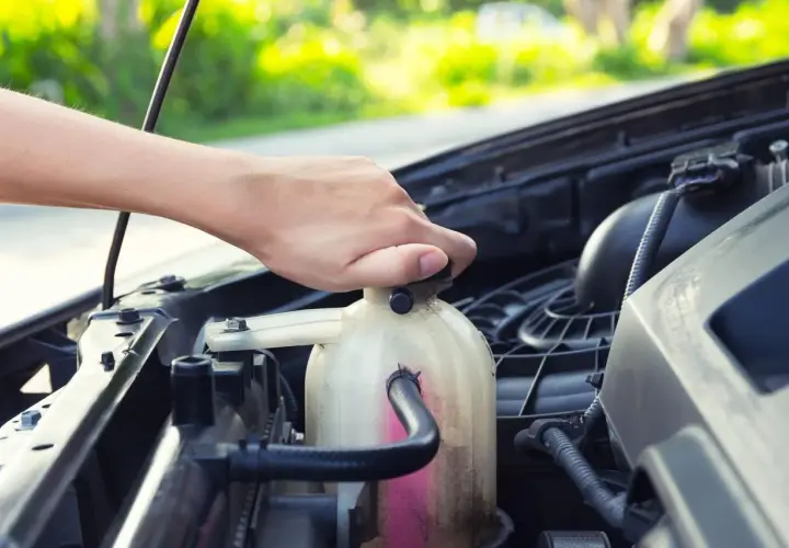 Mano che svita il tappo del serbatoio del liquido refrigerante per la pulizia del radiatore.