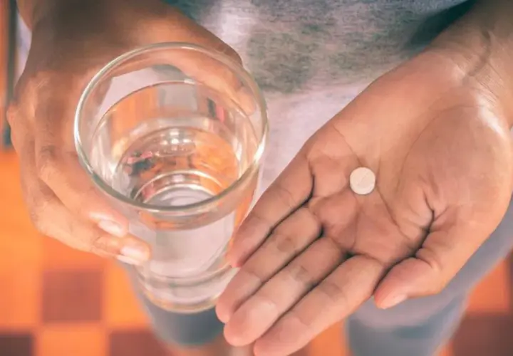 Dłoń trzyma szklankę wody i tabletkę, być może Efferalgan Codeine, by złagodzić ból.