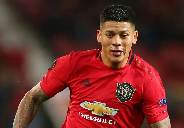 Marcos Rojo w czerwonej koszulce Manchester United, z widocznym logo klubu i sponsora. Jego wiek nie jest widoczny, ale determinacja na twarzy mówi wszystko.
