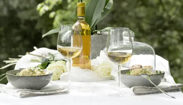 Bordeaux blanc moelleux, deux coupes de vin, deux bols de risotto et des roses blanches sur une table dressée en extérieur.