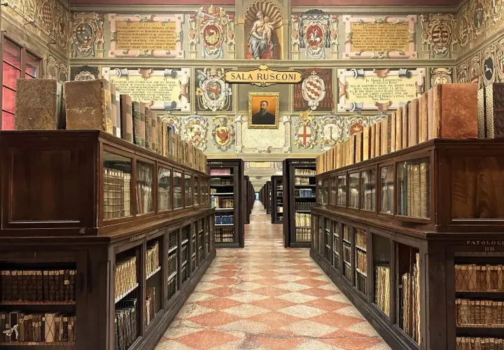 Wnętrze zabytkowej biblioteki z rzędami drewnianych regałów pełnych starych ksiąg, ozdobione malowidłami. To miejsce, gdzie narodziła się nauka, symbolizujące najstarszy uniwersytet na świecie.