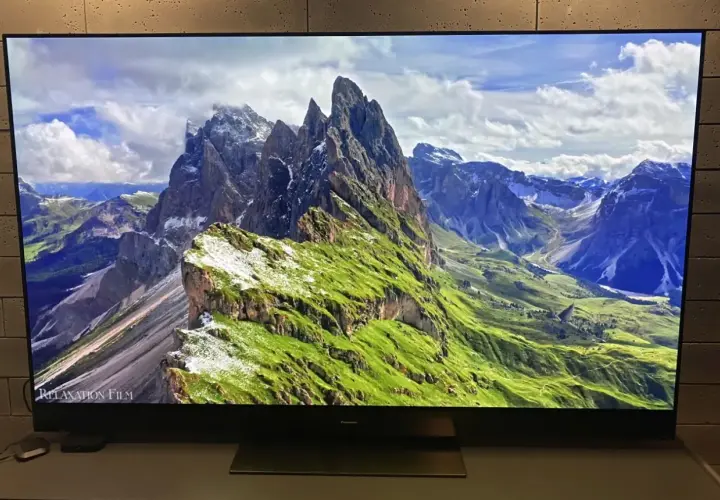 Telewizor wyświetla malowniczy krajobraz górski z zielonymi zboczami i skalistymi szczytami.