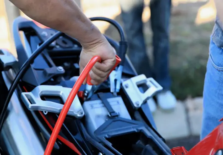 Mano conectando pinza roja para cargar bateria moto.