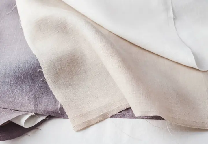 Trois tissus en lin, l'un violet, l'autre beige et le dernier blanc, prêts à blanchir le linge pour un éclat parfait.