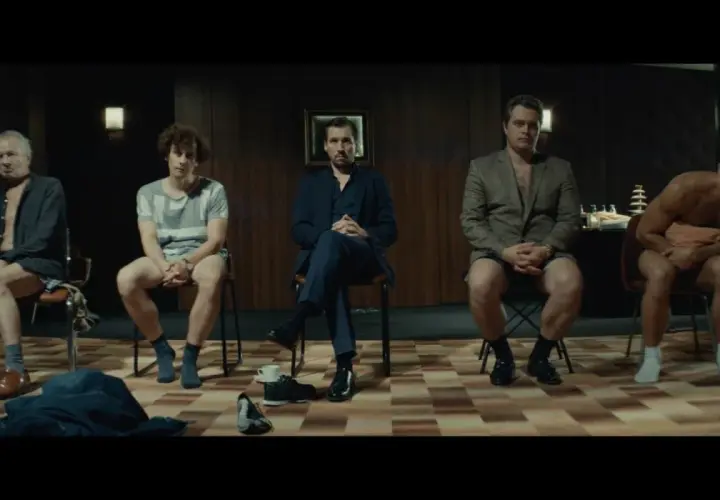 Pięciu mężczyzn siedzi na krzesłach, każdy w innym stroju. Scena z filmu "samiec alfa".