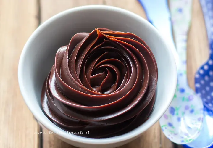 Una spirale di ganache cioccolato per copertura, lucida e invitante, in una ciotola bianca.