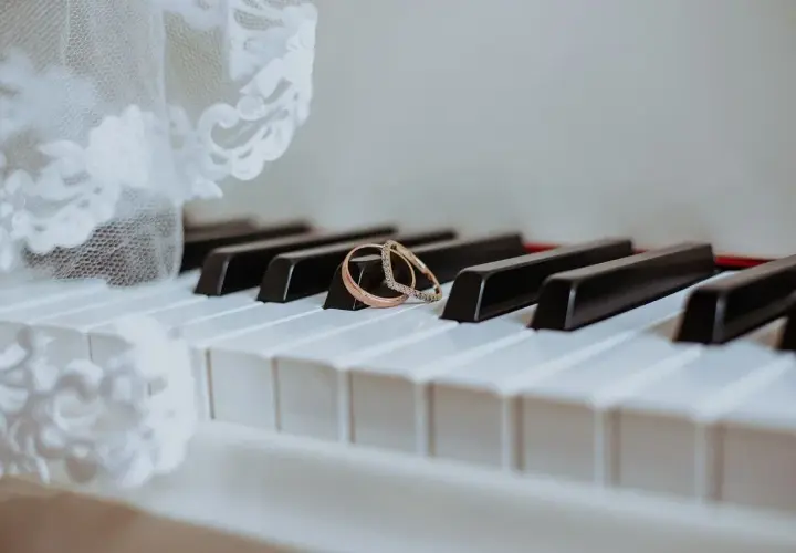 Dwa obrączki na klawiszach pianina, obok białej koronki.