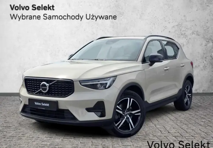 Jasny beżowy Volvo XC40, używane z salonu, prezentuje się elegancko na tle betonowej ściany.