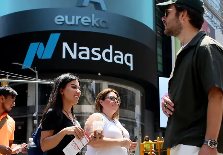 Ludzie przed budynkiem Nasdaq, gdzie handluje się akcjami. Słońce świeci, tworząc cień.