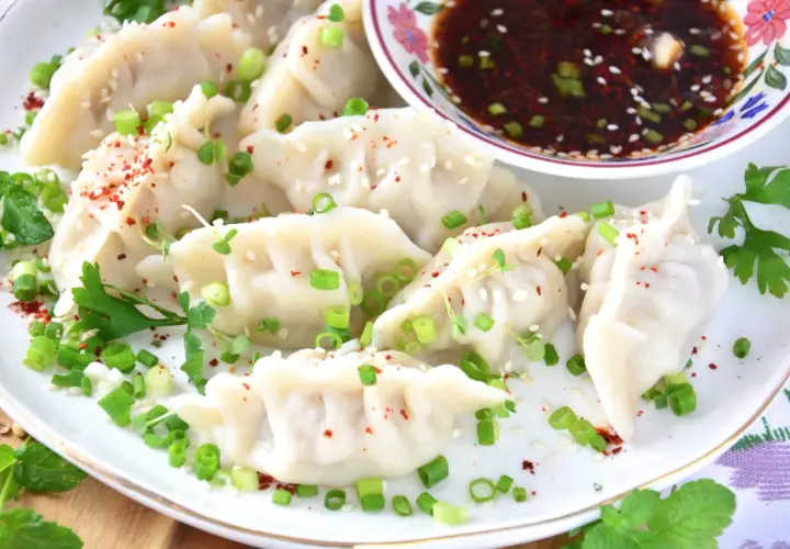 Pyszne pierożki gyoza posypane szczypiorkiem i sezamem, gotowe do zanurzenia w sosie.