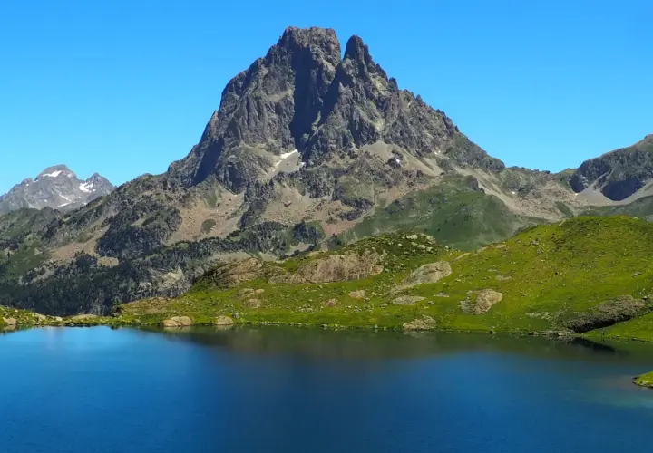 Lago azul intenso reflejando picos rocosos y verdes laderas en los Pirineos Francia.