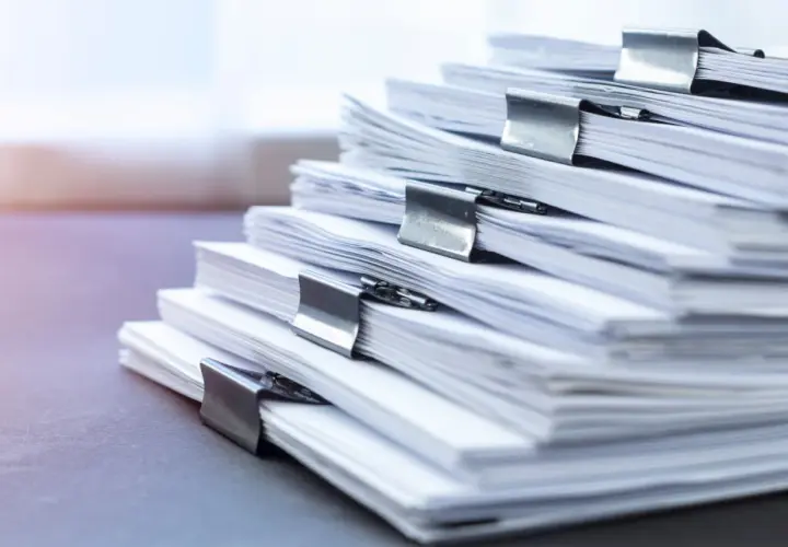 Stos dokumentów z klamrami. Zastanawiasz się, jakie dokumenty są potrzebne do sprzedaży działki rolnej? Oto stos papierów, które mogą być kluczowe.