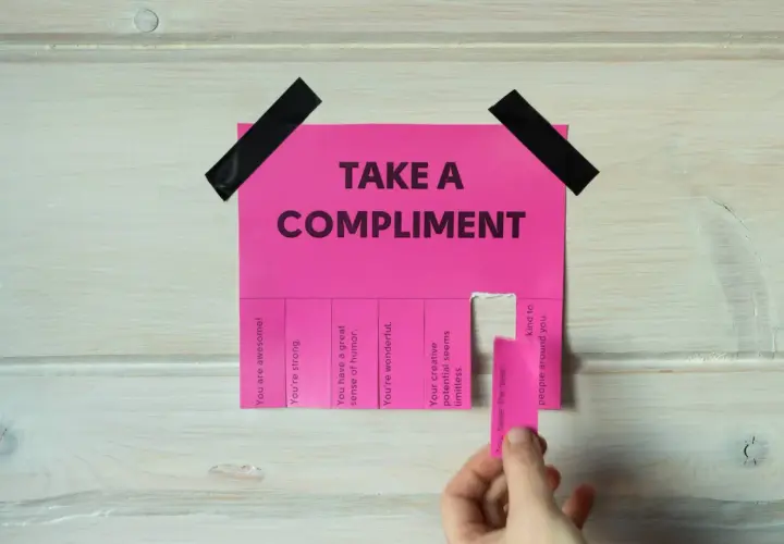 Różowa kartka z napisem "TAKE A COMPLIMENT" i odrywanymi kuponami z pochwałami. Daje to pomysł na inteligentne odpowiedzi na komplementy.