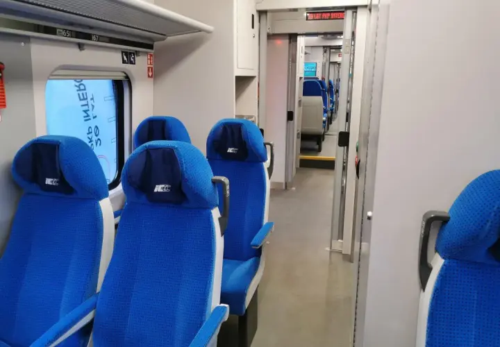 Wnętrze pociągu ed74 z niebieskimi siedzeniami i przejściem.