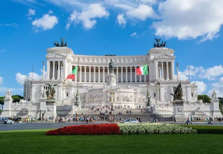Il Vittoriano, uno dei monumenti famosi di Roma, con bandiere italiane e cielo azzurro.