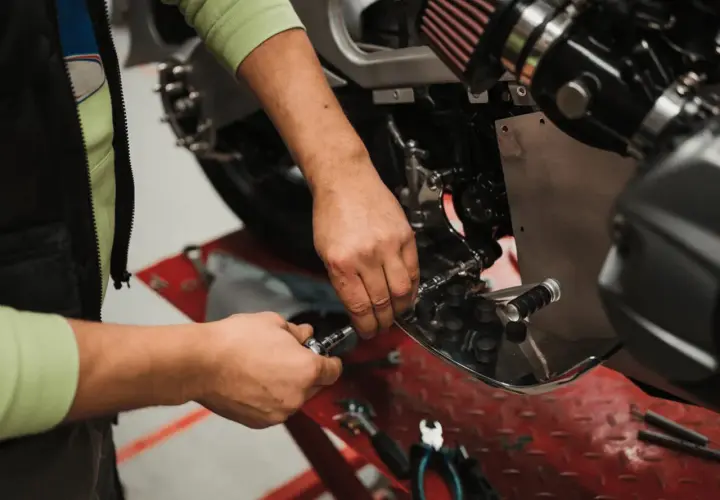 Mecánico realizando el cambio de aceite a una moto, usando herramientas para acceder al motor.