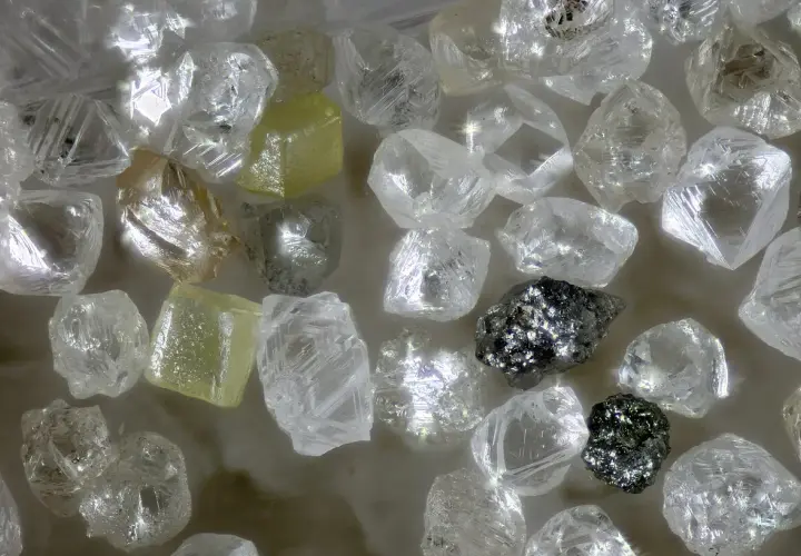 Unbearbeitete Diamanten, einige gelblich, andere klar, glänzen. Ihre Seltenheit und Härte erklären, warum sind Diamanten so wertvoll.
