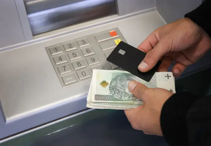 Ręce trzymające kartę i banknoty przy bankomacie, pokazujące, jak wpłacić pieniądze na konto.