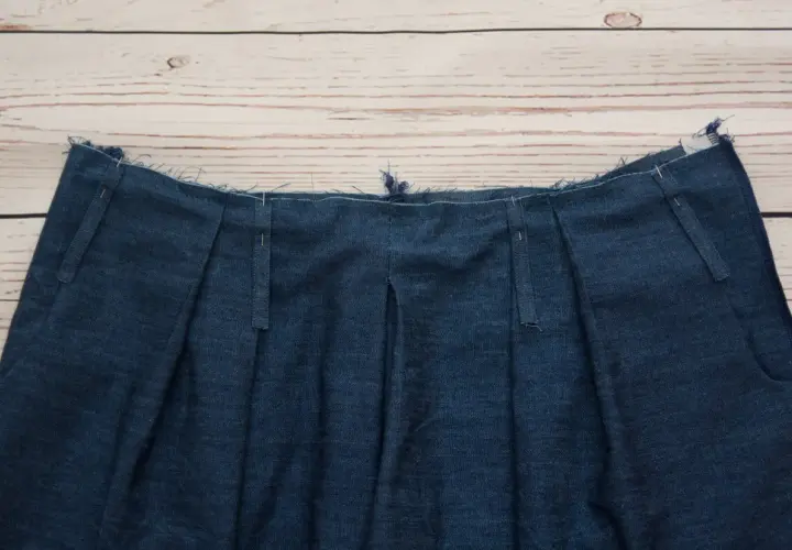 Close-up of a denim garment's waistband, showcasing various types of belt loops being prepared for sewing.