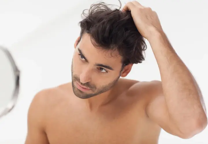 Hombre revisando su cabello en el espejo, parte de su rutina de cuidado del cabello hombre.