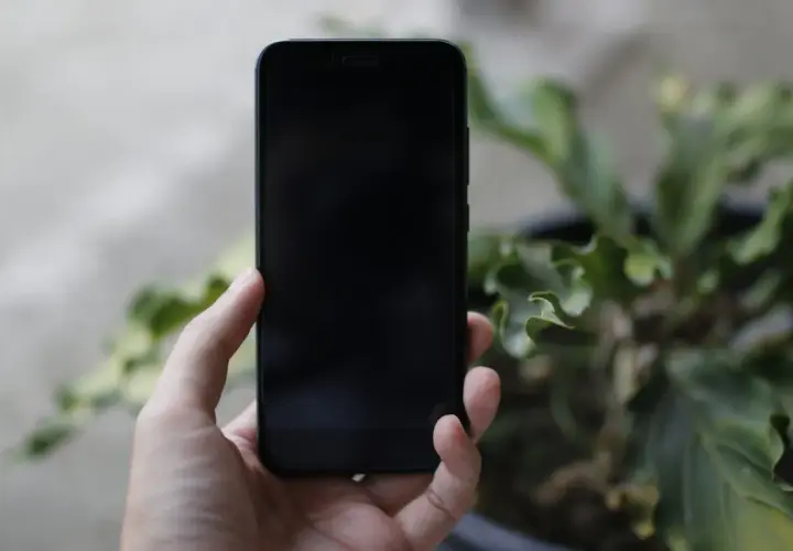 Dłoń trzyma czarny iPhone. Zastanawiasz się, jak wyłączyć iPhone bez dotyku?