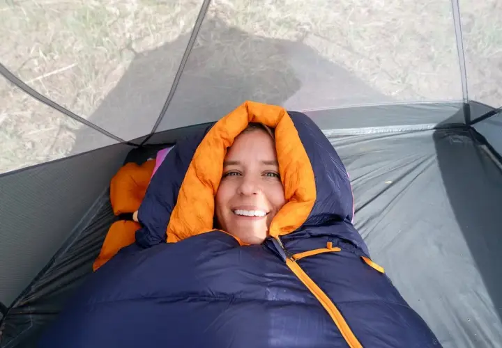 Smiling woman bundled in a navy and orange rei magma 15 weight sleeping bag inside a tent.