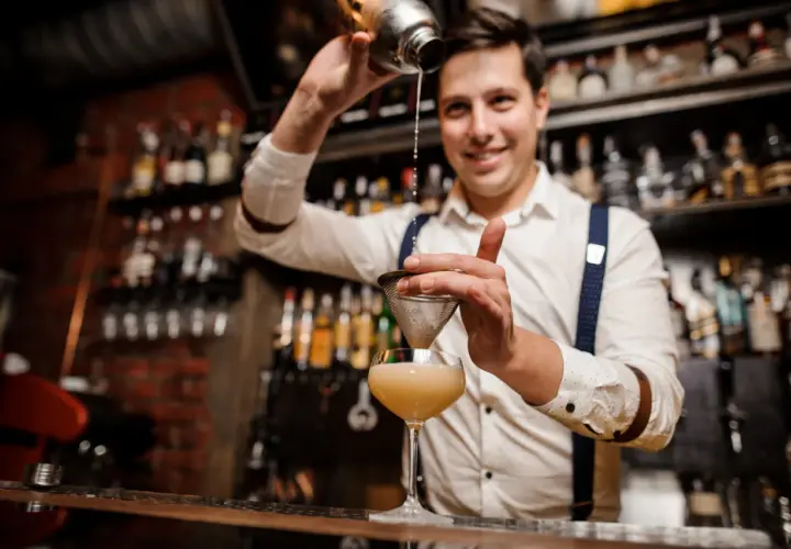 Uśmiechnięty barman przelewa drinka przez sitko. Czy barman może pić w pracy? Ten z pewnością tworzy pyszne koktajle!